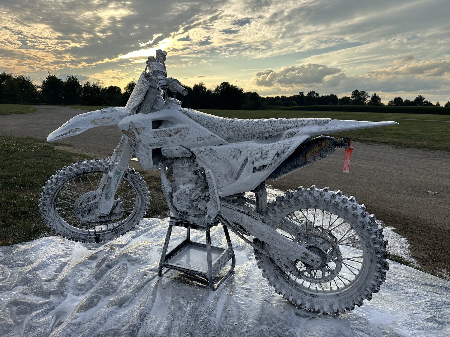 A motocross bike covered head to toe in wash foam on a stand at sunset