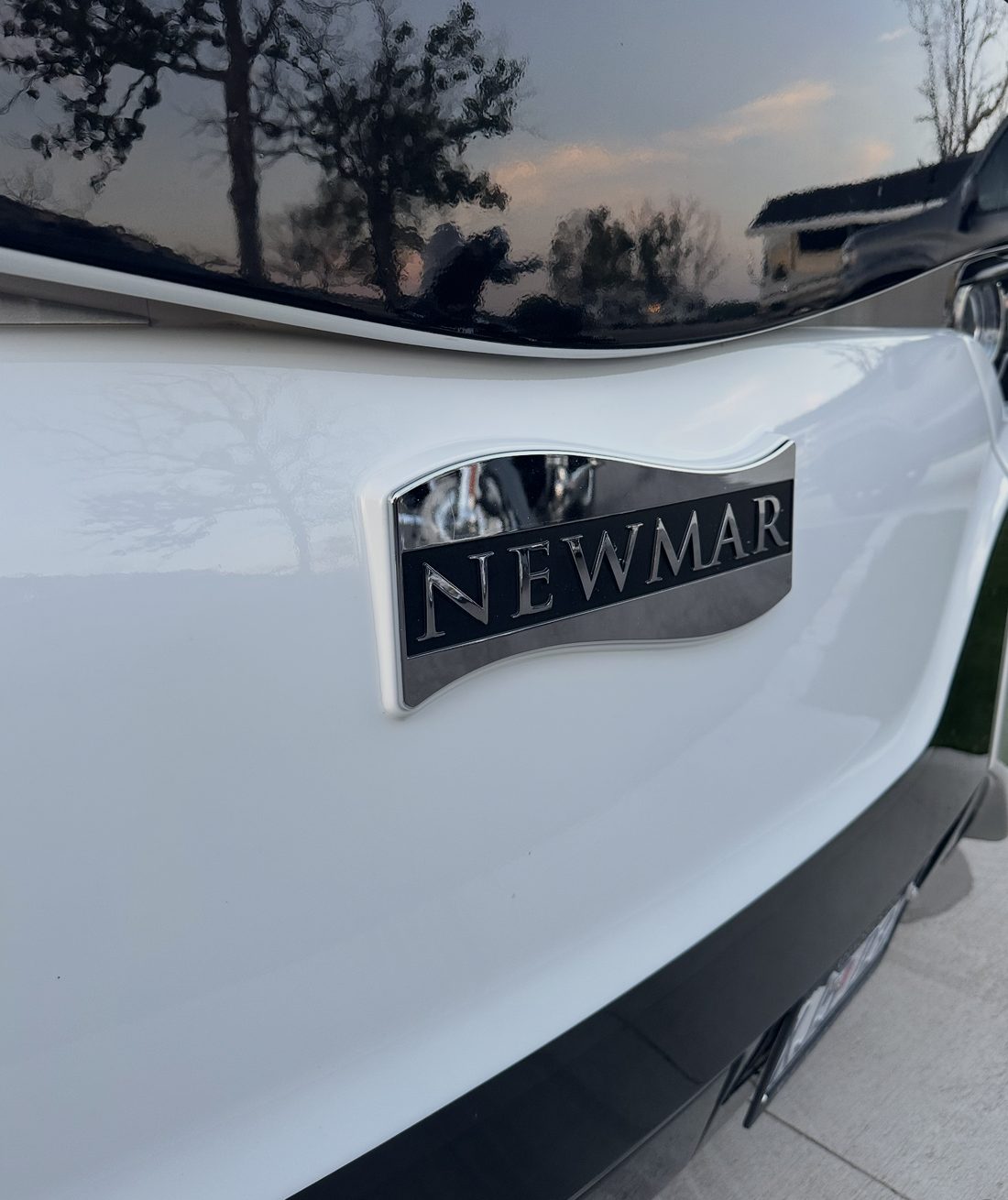 A white Newmar coach front cap washed to a spotless, mirror finish that reflects the trees and sky